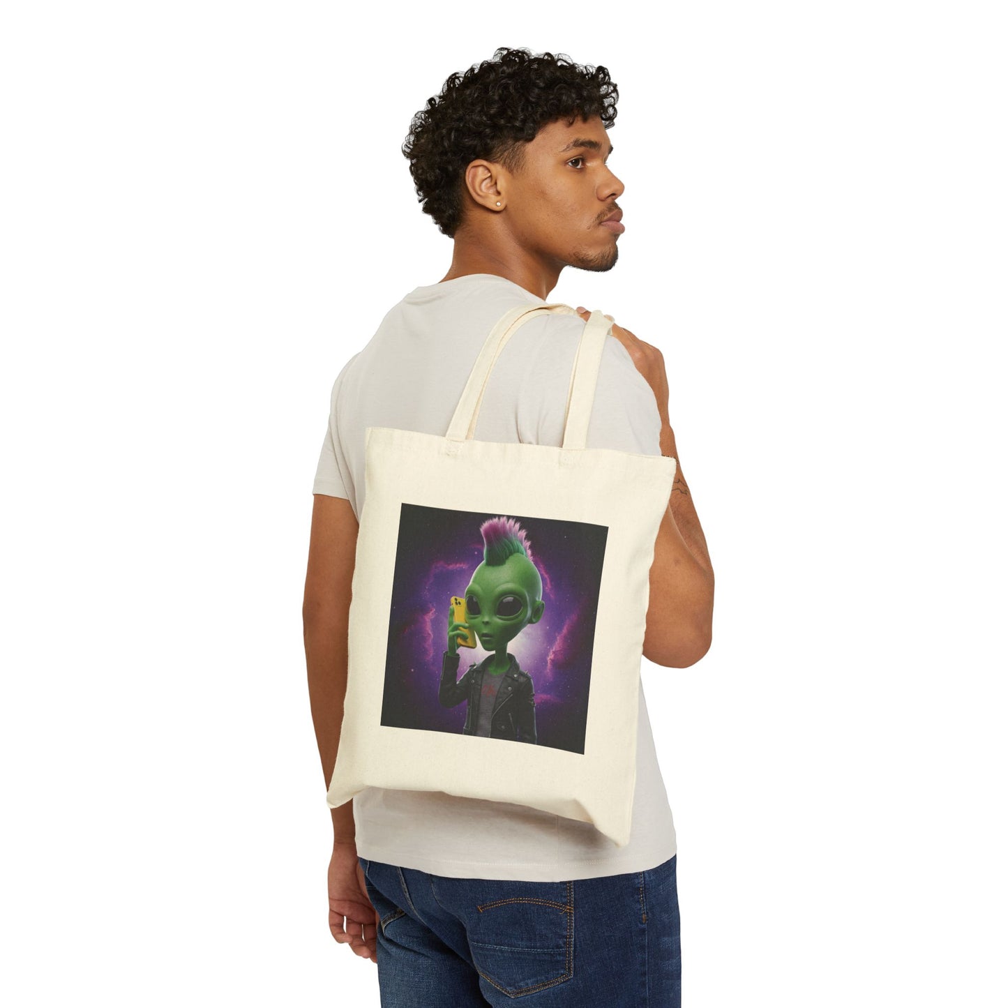 A punk-styled green alien with a pink and green mohawk wearing a leather jacket and holding a yellow mobile phone. The alien Is featured on a spacious Natural tote bag wearing on a young man shoulder..