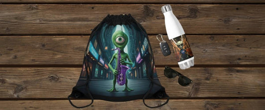A top-down mockup on a wooden background showing a black drawstring bag with a green one-eyed alien playing a purple saxophone, next to an insulated water bottle, sunglasses, and car keys.