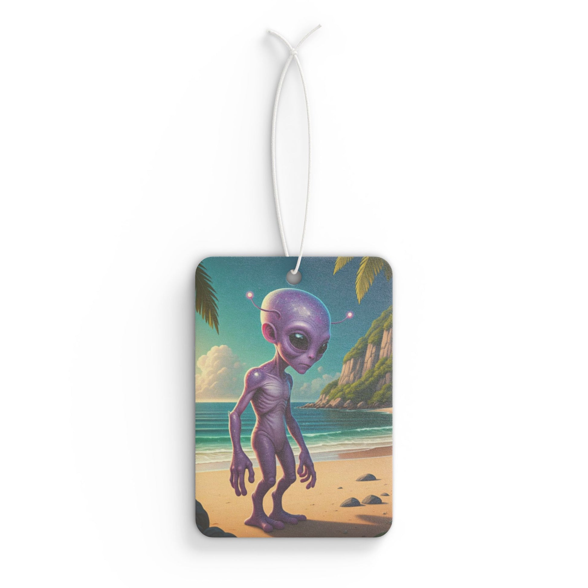 Rectangular car air freshener showing a tall, purple alien standing on a sandy tropical beach with ocean waves and green palm leaves overhead.