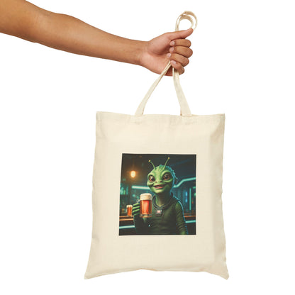 Alien woman drinking a Beer in a pub at night. The alien Is featured on a Natural color Canvas tote bag.