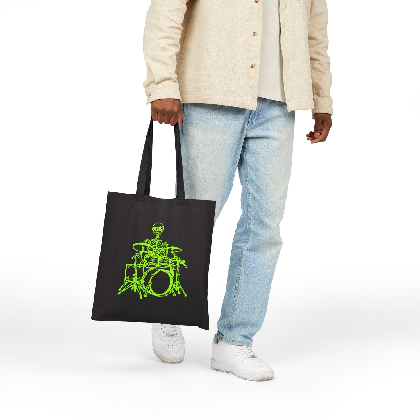 Person holding a black tote bag with a unique green skeleton playing drums design