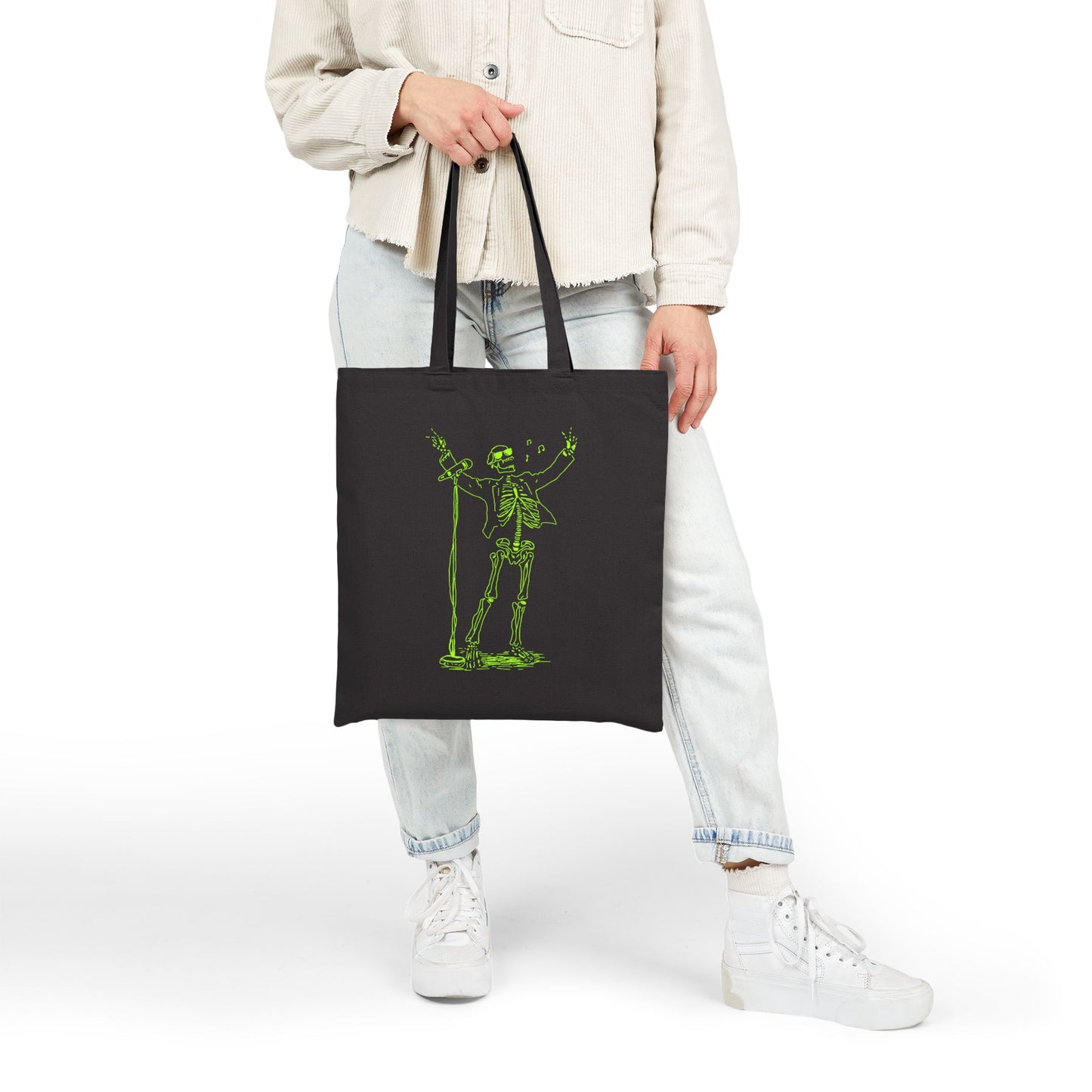 Person holding a black tote bag with a green skeleton design on a white background