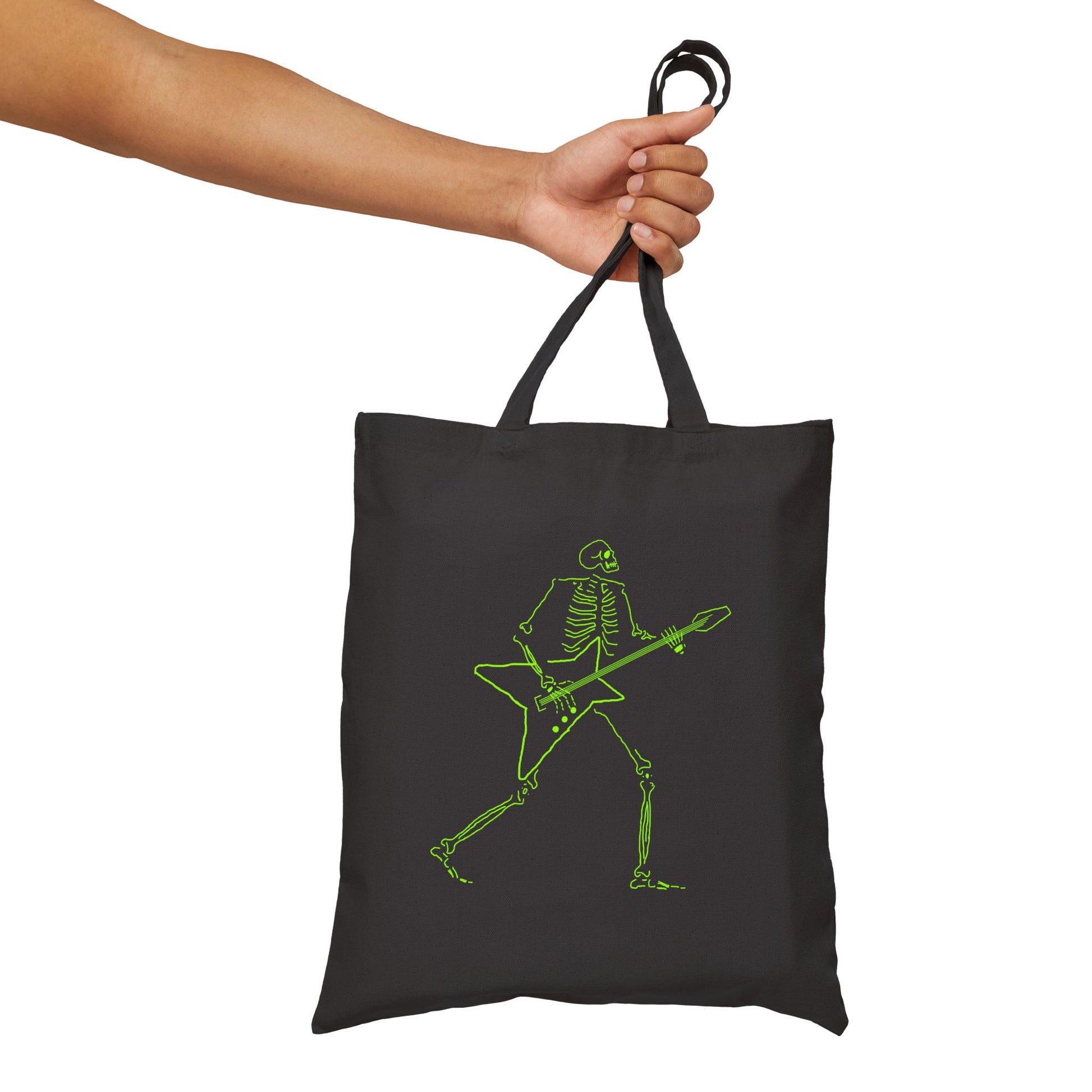Black tote bag with green skeleton playing guitar design held by a hand on a white background