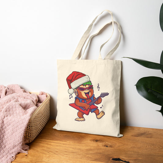 Tote bag with a monkey playing guitar and wearing a Santa hat on a wooden surface.