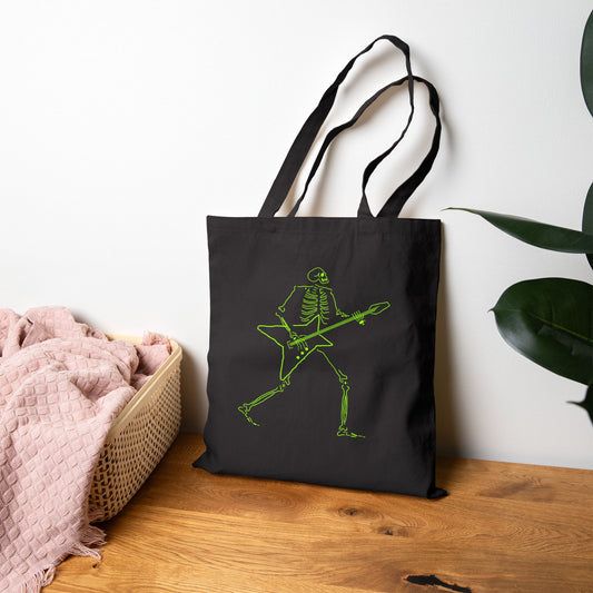 Black tote bag with a green skeleton playing guitar design on a wooden surface.