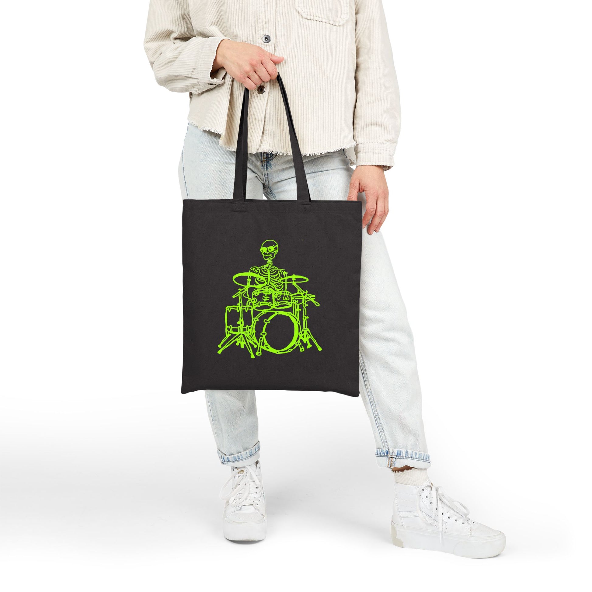 Person holding a black tote bag with a unique  green skeleton and drum set design