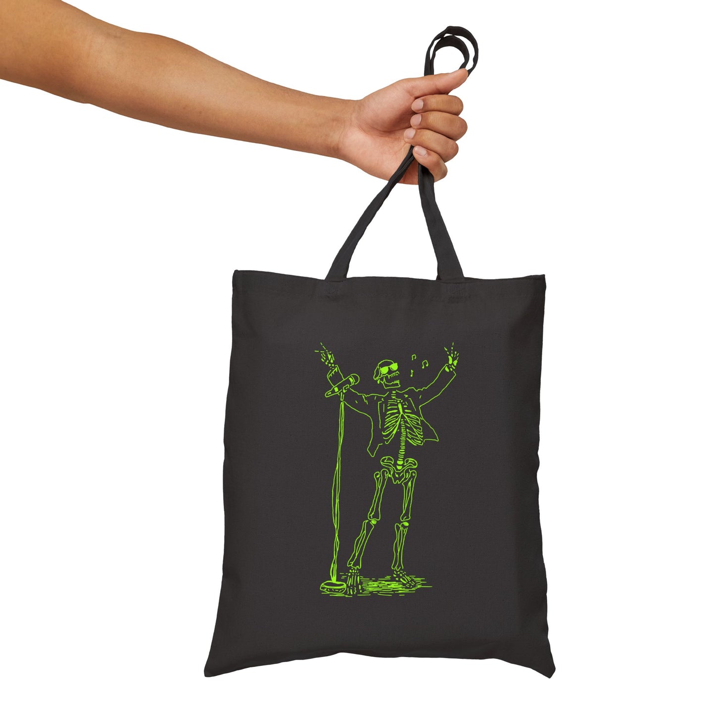 Black tote bag with unique green skeleton design held by a hand