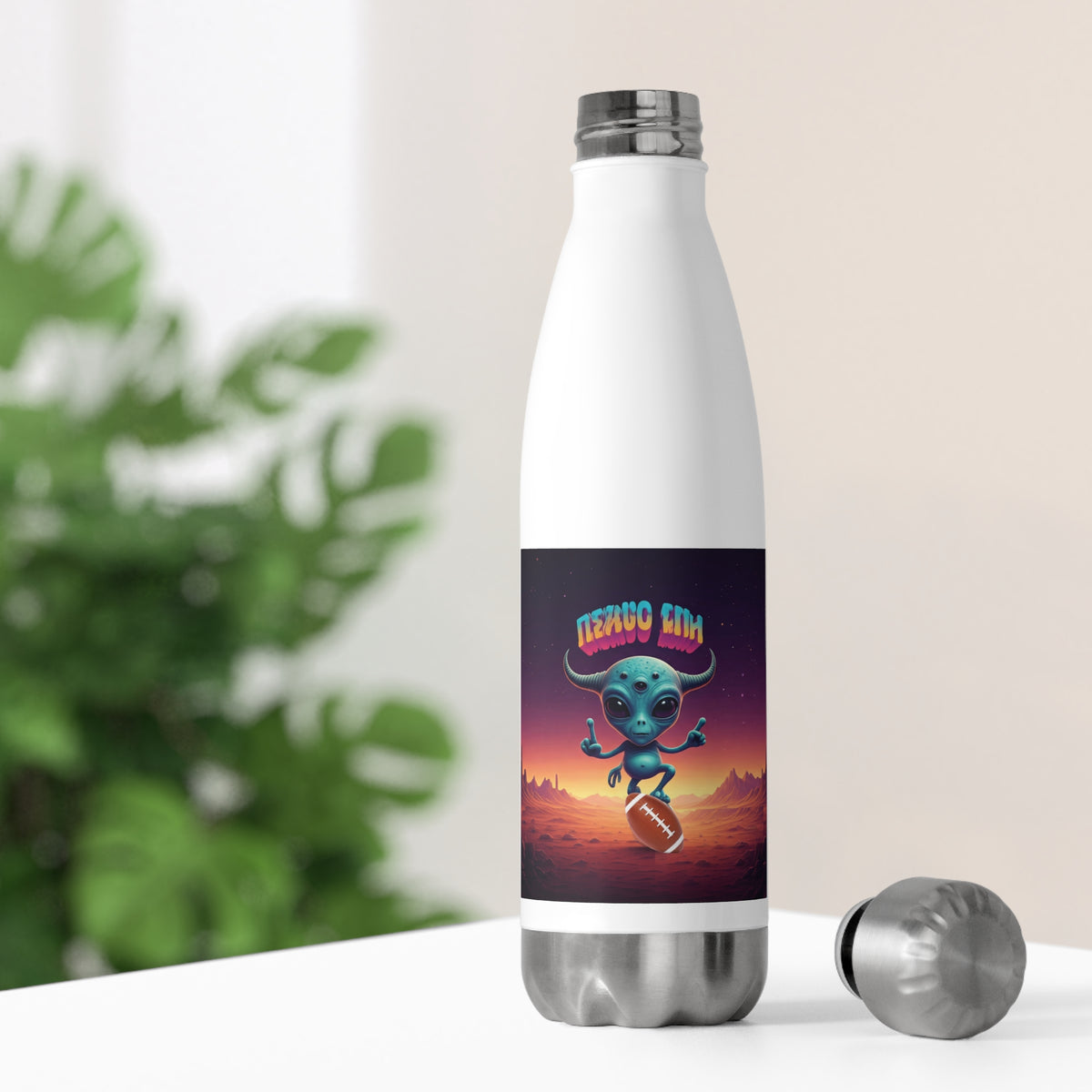 White thermal sports water bottle on a desk with its silver stainless steel cap off, showing a cosmic football alien design for office and gym use.