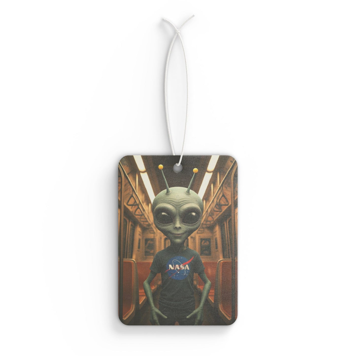 Rectangular car air freshener featuring a grey alien wearing a NASA t-shirt, standing inside a vintage subway train car.
