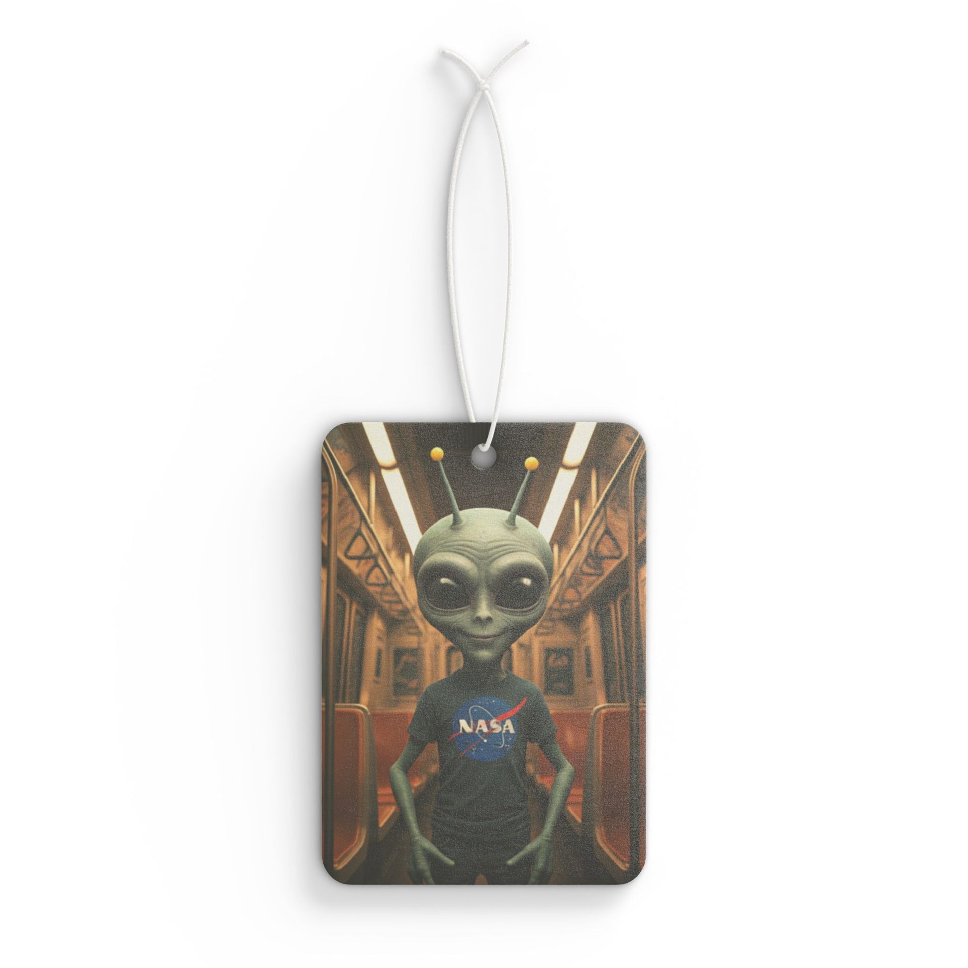 Rectangular car air freshener featuring a grey alien wearing a NASA t-shirt, standing inside a vintage subway train car.