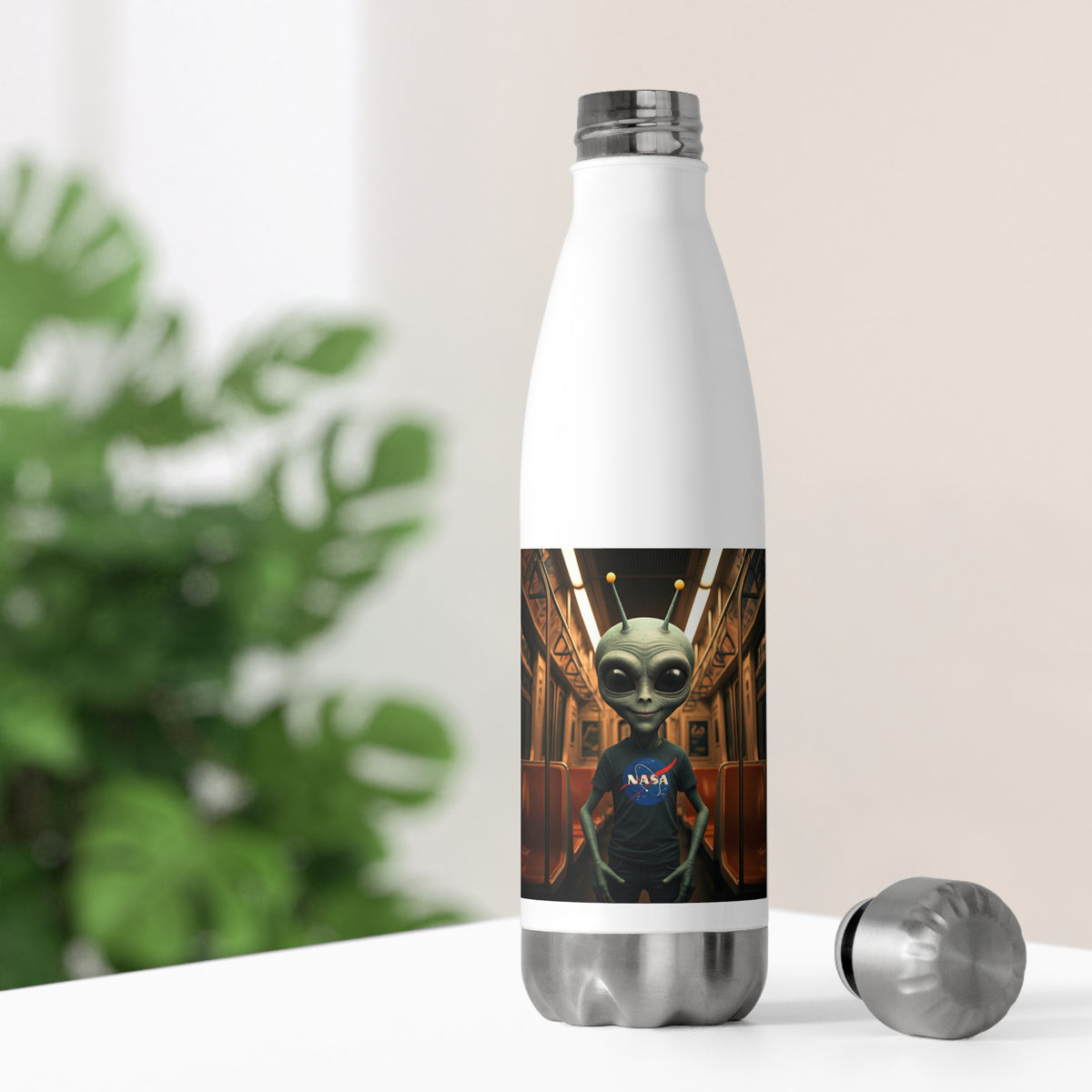 White thermal travel water bottle sitting on a desk with its silver stainless steel cap off, showing an alien subway commuter artwork for office hydration.