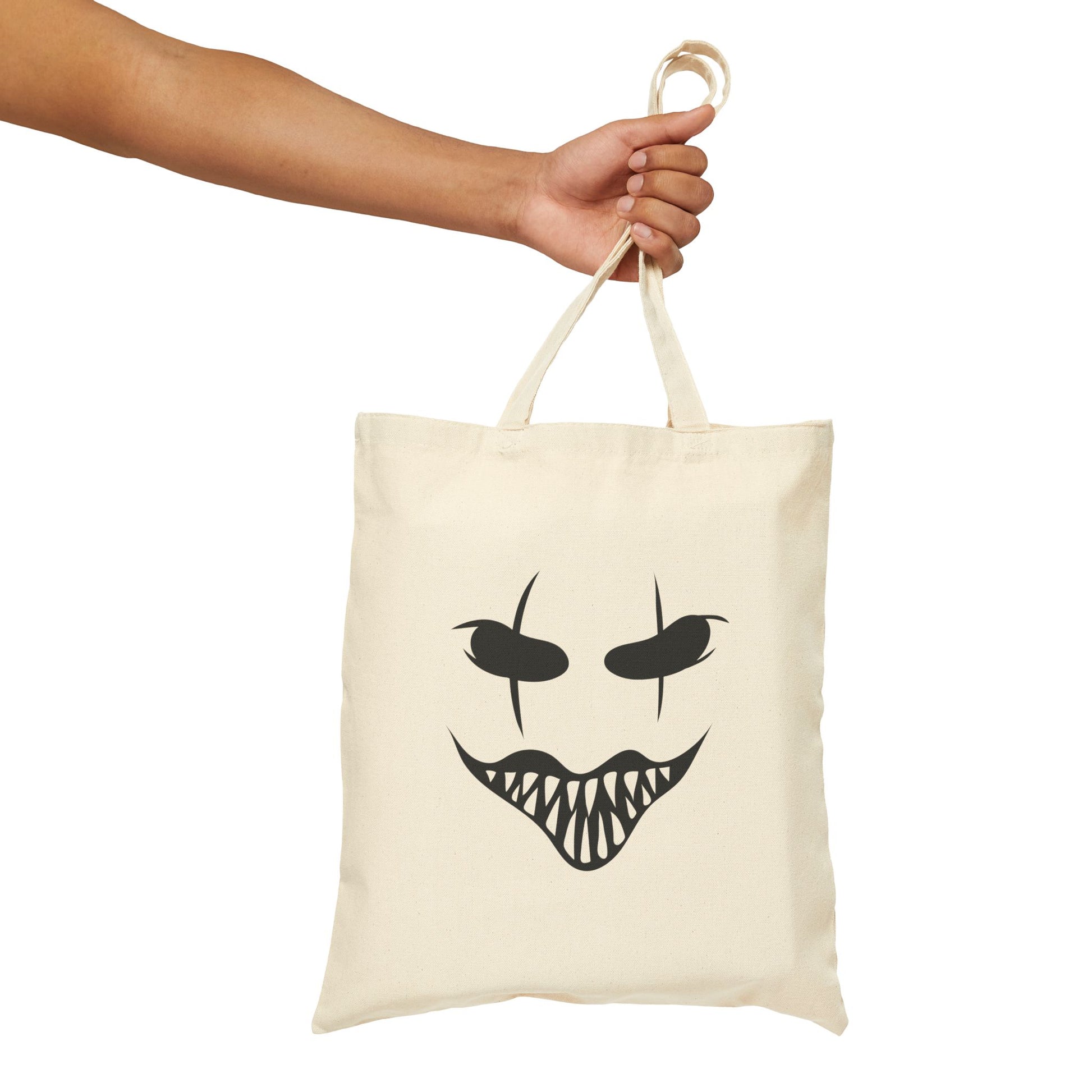 Tote bag with a black face design held by a hand on a white background