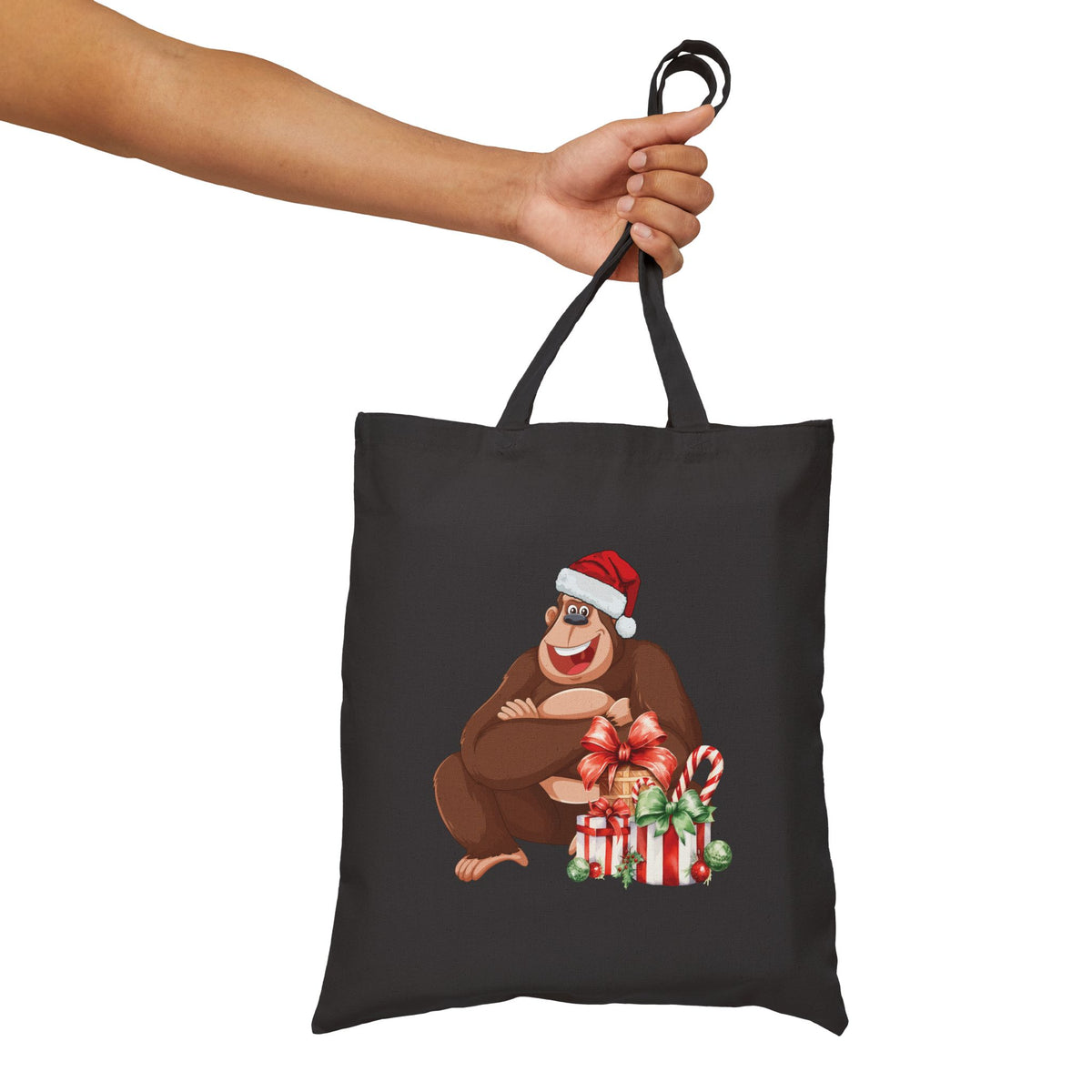 Black canvas tote bag held in hand featuring a happy Santa gorilla graphic with holiday gifts for festive daily errands and Christmas shopping.   