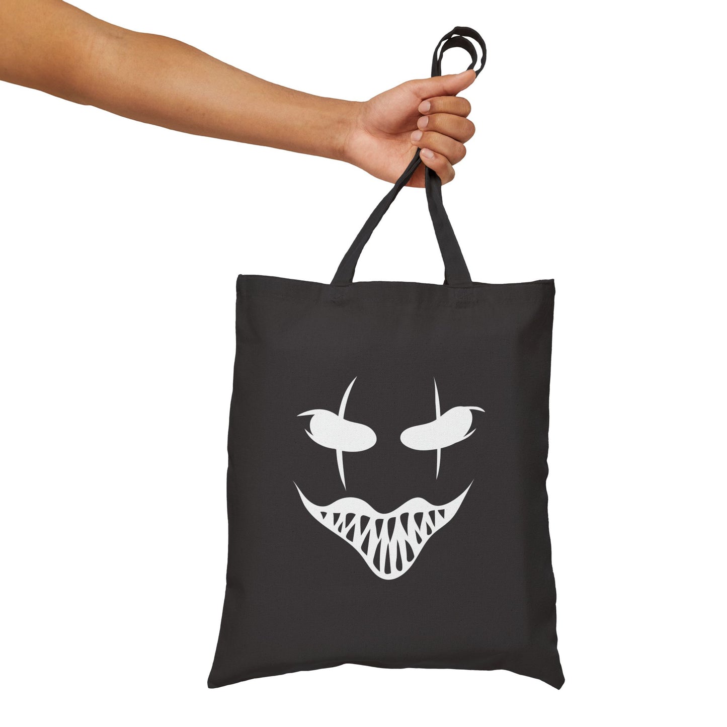 Black tote bag with a white face design held by a hand on a white background