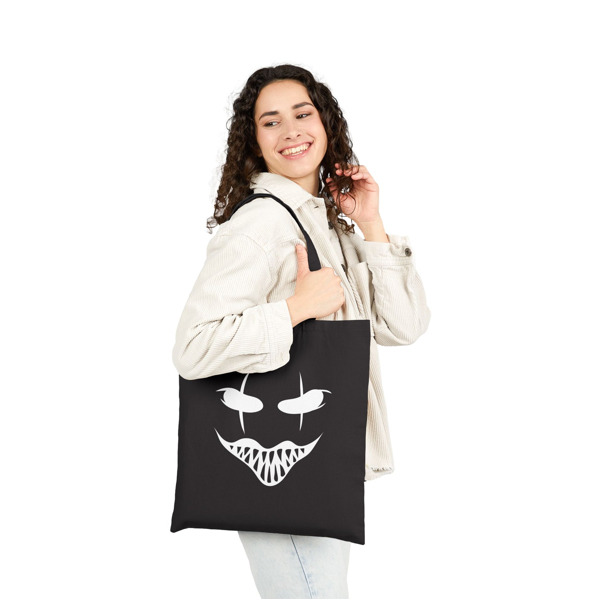 Person holding a black tote bag with a white face design on a white background