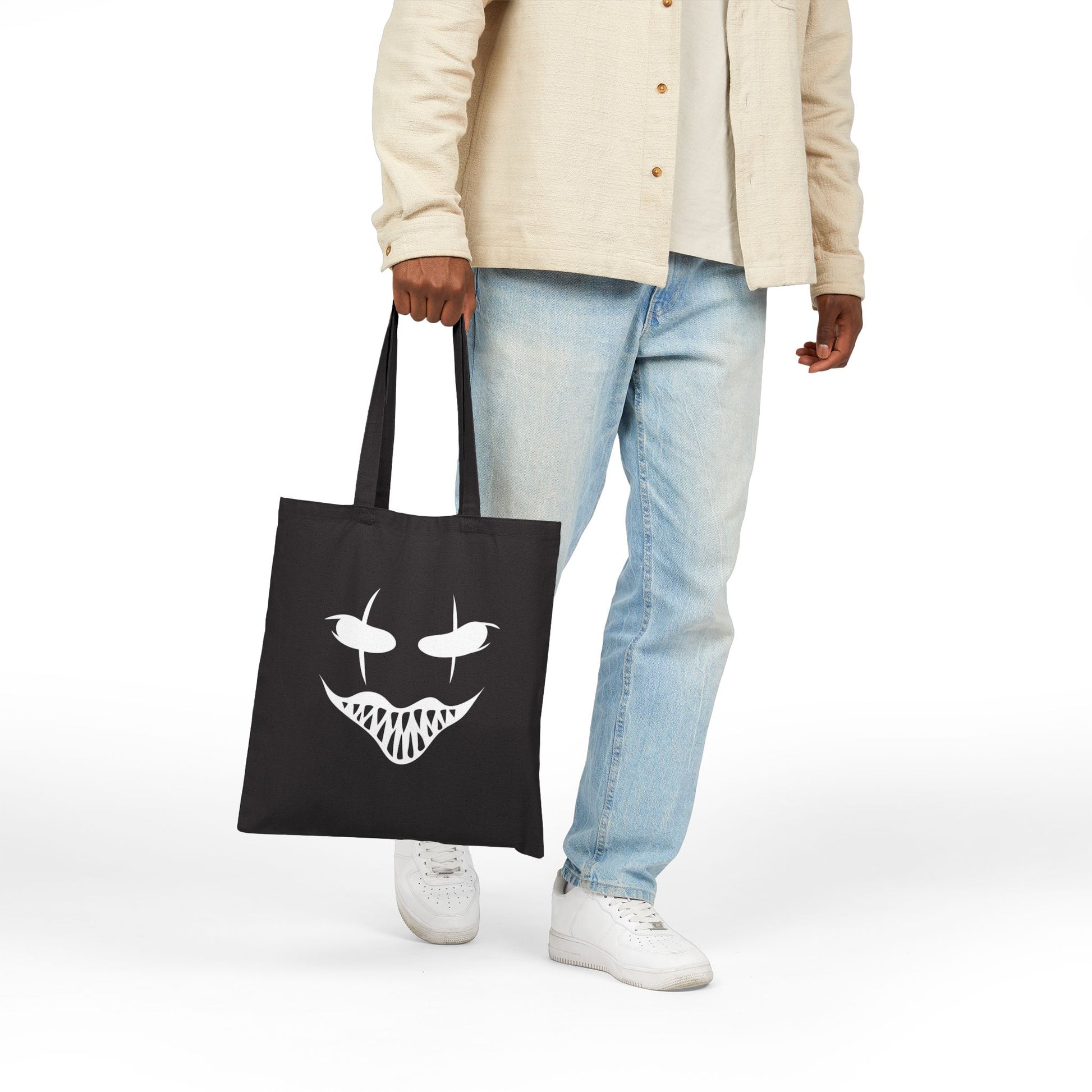 Person holding a black tote bag with a white face design on a white background