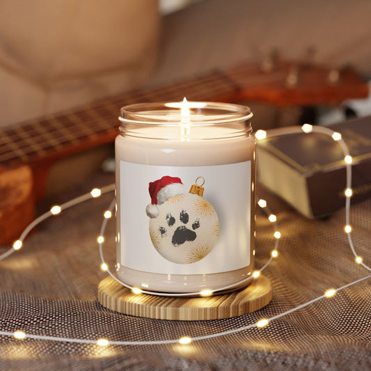 Lit soy wax glass jar Christmas candle with Santa hat dog paw print ornament label, glowing with fairy lights on a cozy wooden table near a guitar.