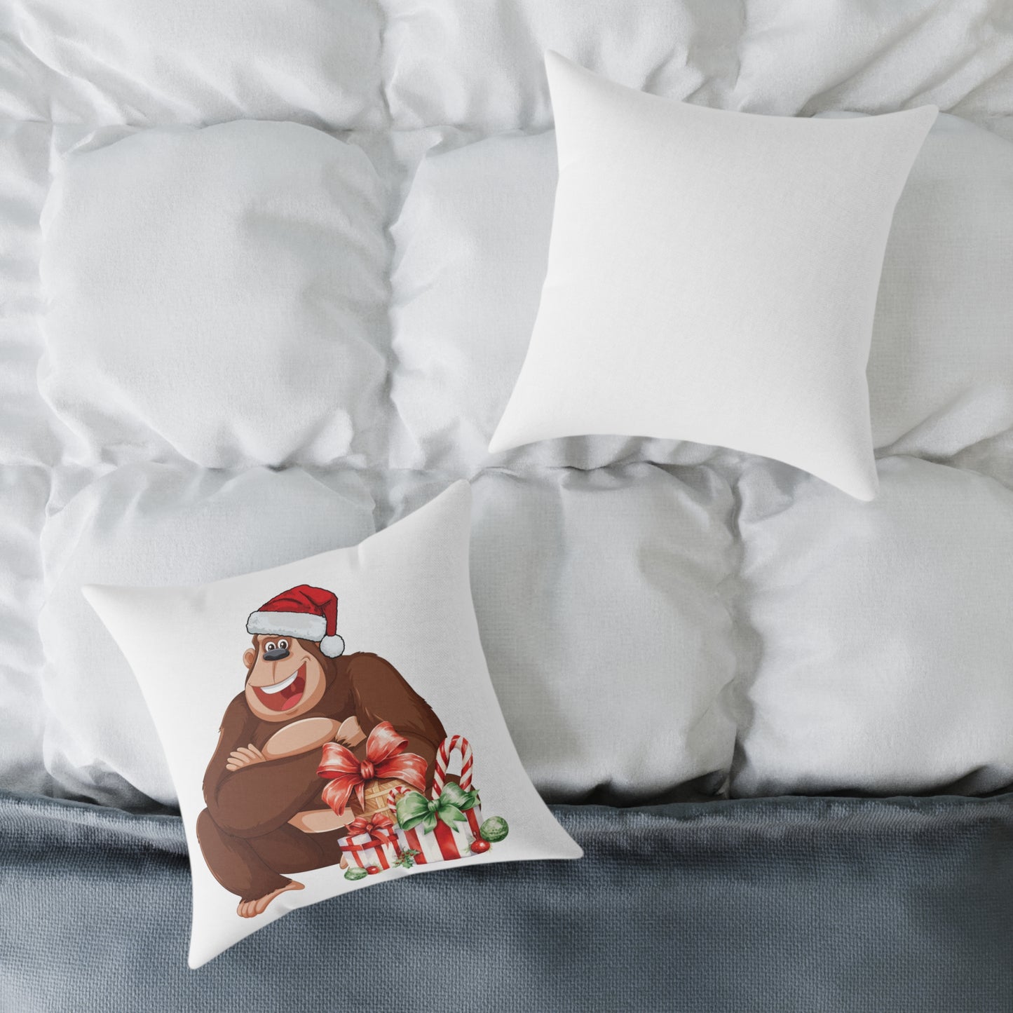 Decorative pillow with a bear wearing a Santa hat and holding Christmas gifts on a bed with white pillows and gray bedding.