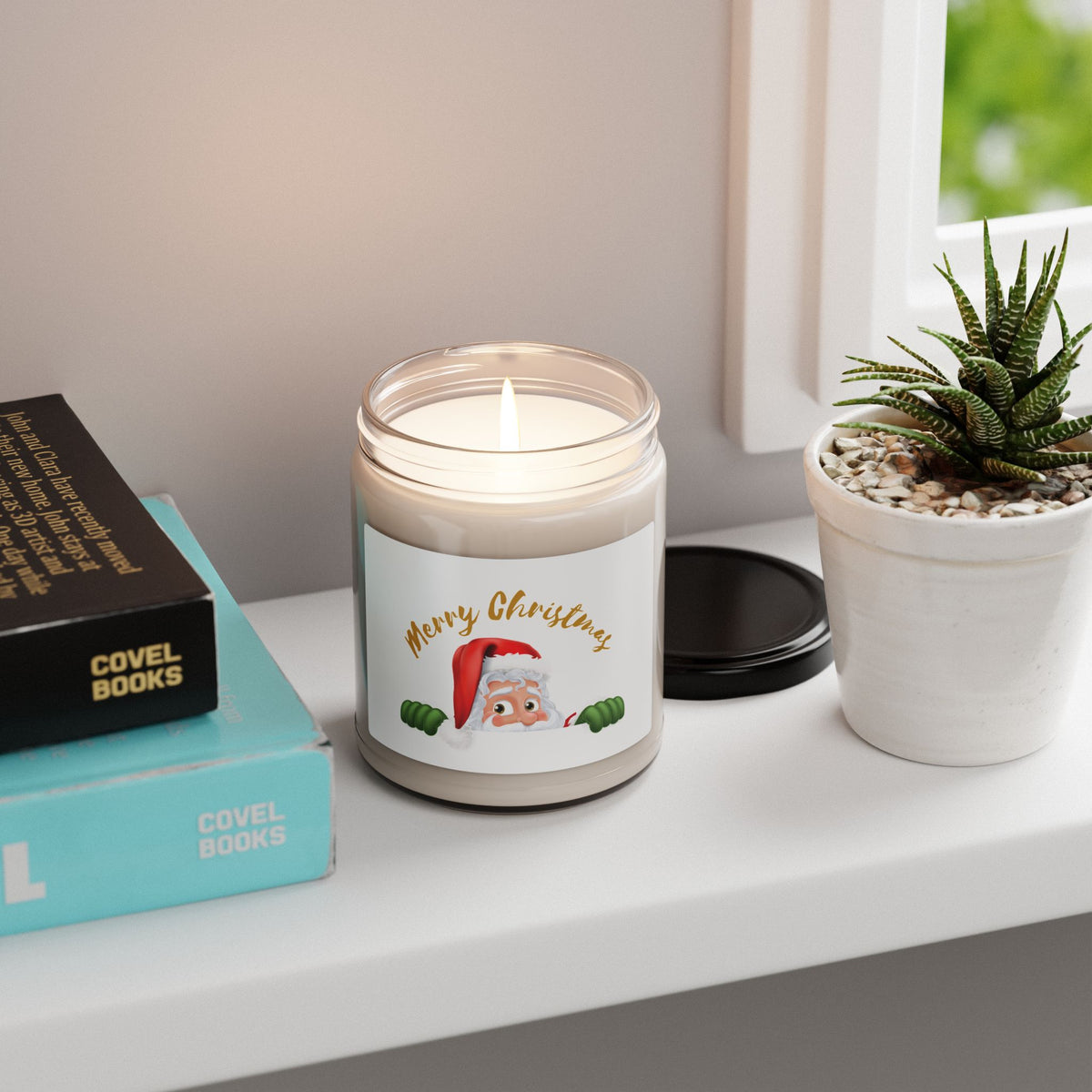 Scented Christmas soy candle with a playful peeking Santa Claus graphic placed on a bright windowsill next to books and a potted succulent.