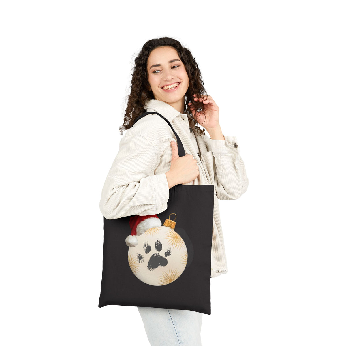 Woman wearing white jacket carrying a black dog mom santa paws ornament tote bag for festive christmas gift shopping