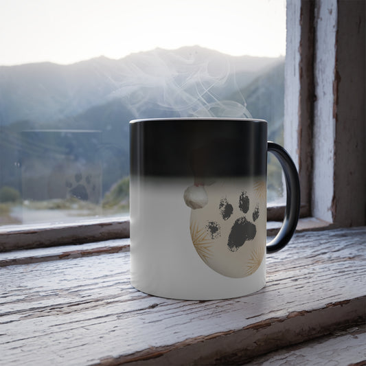 Heat sensitive color changing mug revealing a dog paw print christmas bauble with a Santa hat on a rustic wooden windowsill with a mountain view.