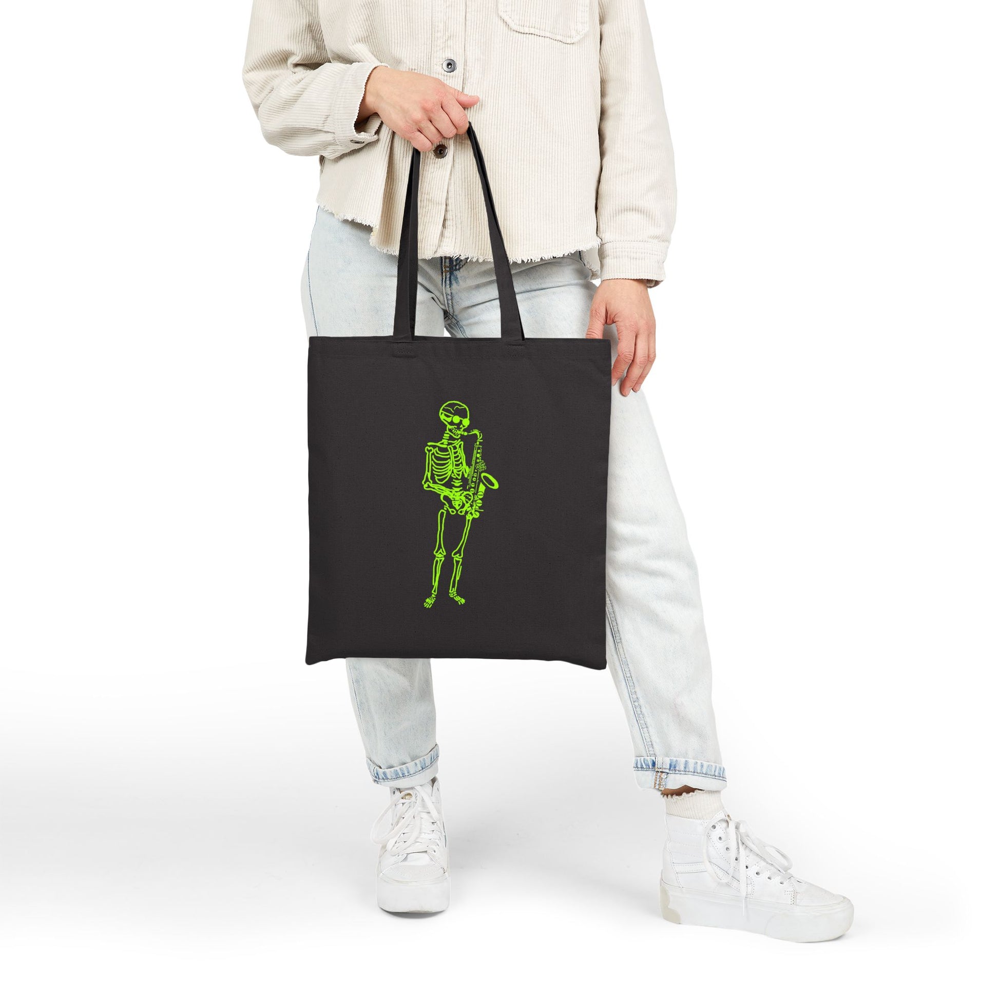 Person holding a black tote bag with a green sax player skeleton design
