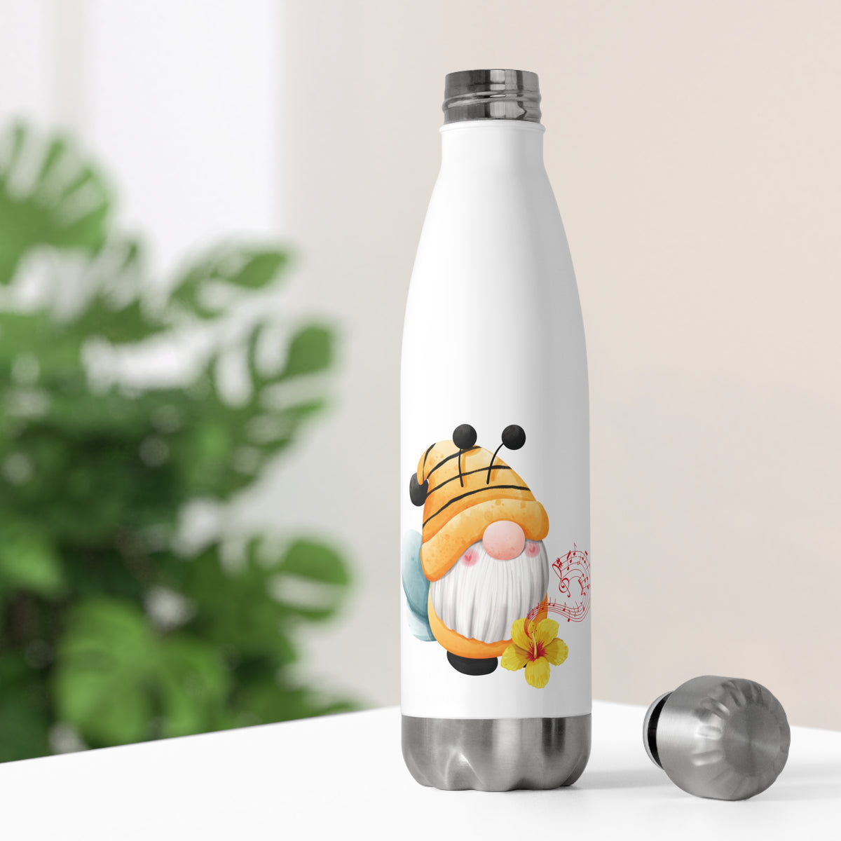 White insulated stainless steel water bottle printed with a charming bumblebee hat gnome graphic and blossom flower, standing on a table with its screw lid open next to houseplants.