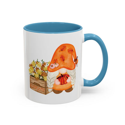 White and light blue ceramic coffee mug with a colorful graphic of a mysterious gnome surrounded by autumn leaves and mushrooms.