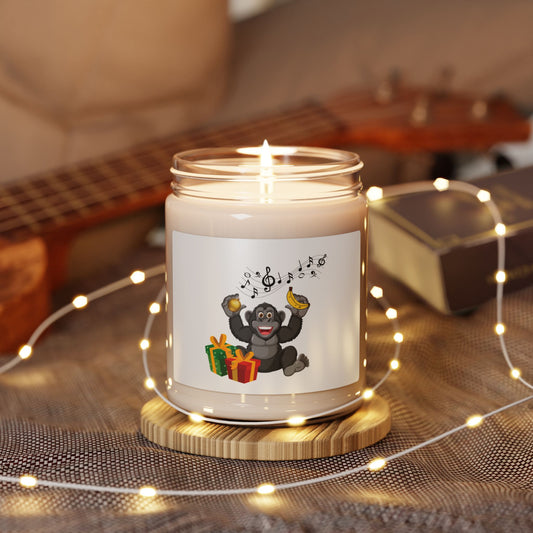 Lit soy wax glass jar Christmas candle featuring a cheerful gorilla with music notes, holding bananas above holiday gift boxes, glowing with fairy lights on a wooden table next to a guitar.
