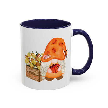 White and navy ceramic coffee mug with a colorful graphic of a mysterious gnome surrounded by autumn leaves and mushrooms.