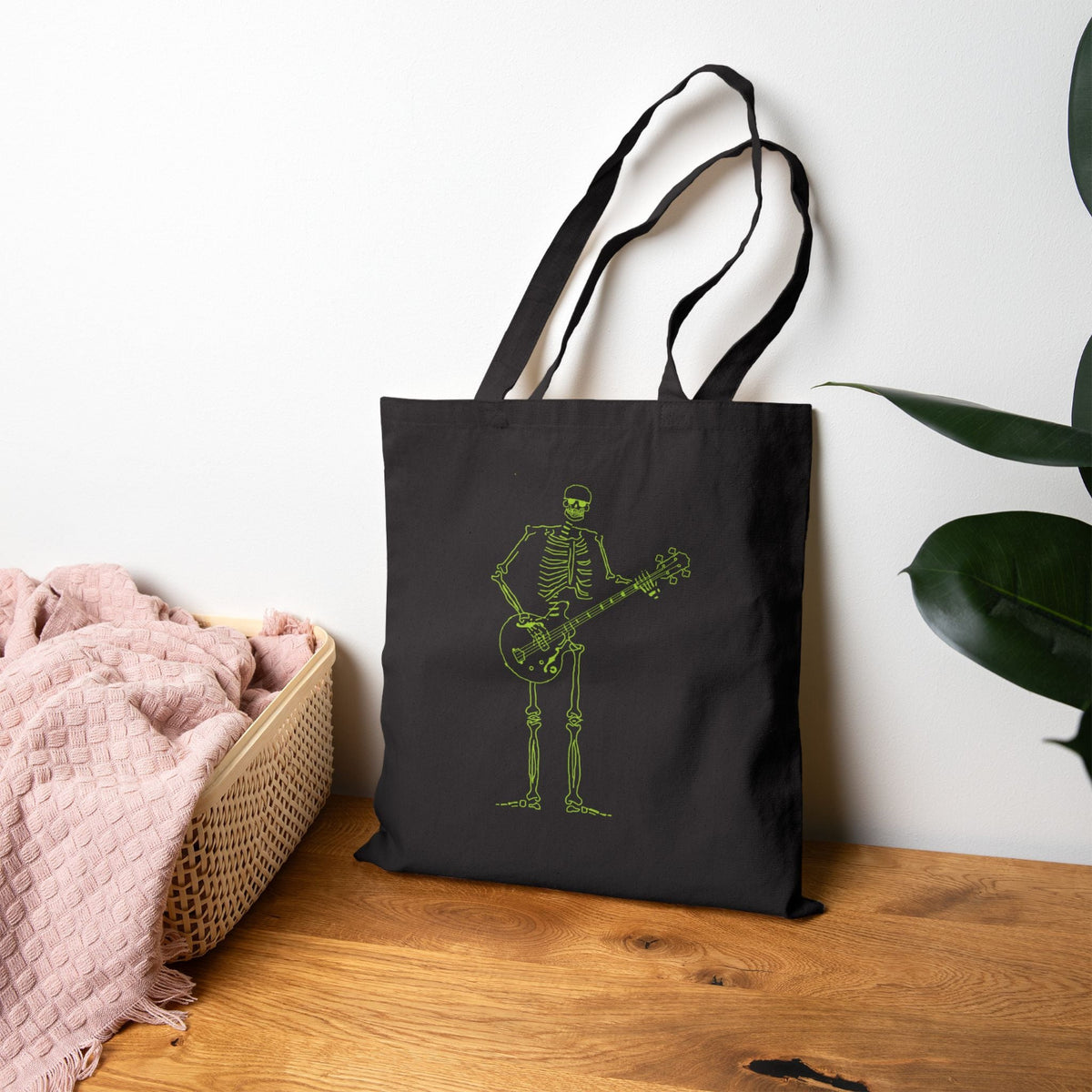Black eco-friendly tote bag printed with a glowing neon skeleton playing electric guitar.