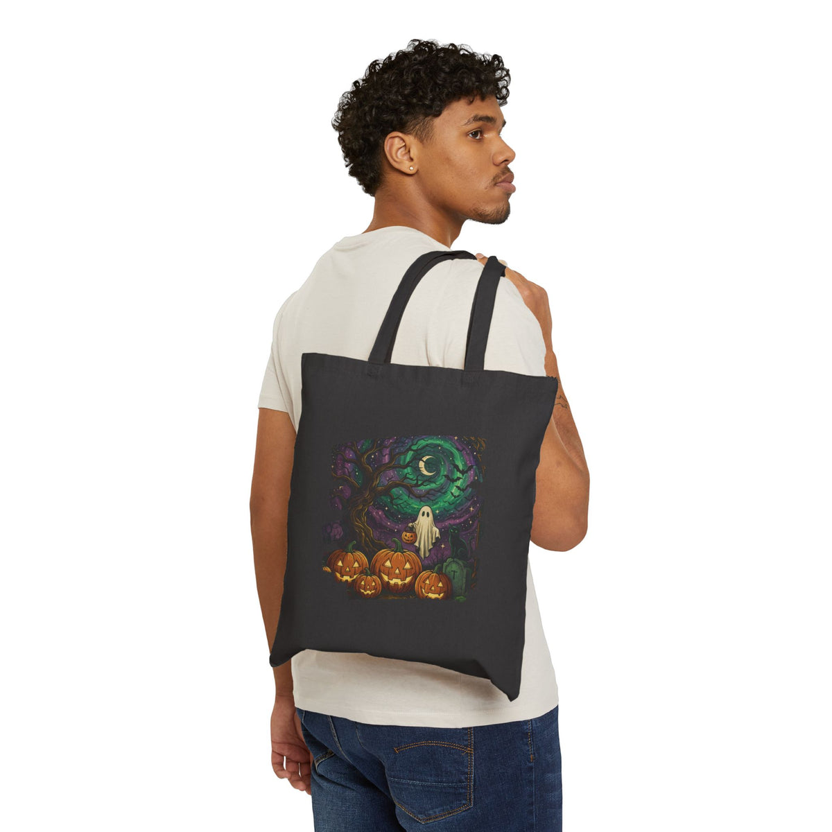 Black canvas tote bag with exclusive Halloween ghost, pumpkins, and spiral moon art from From Space Store on a cozy wooden surface.