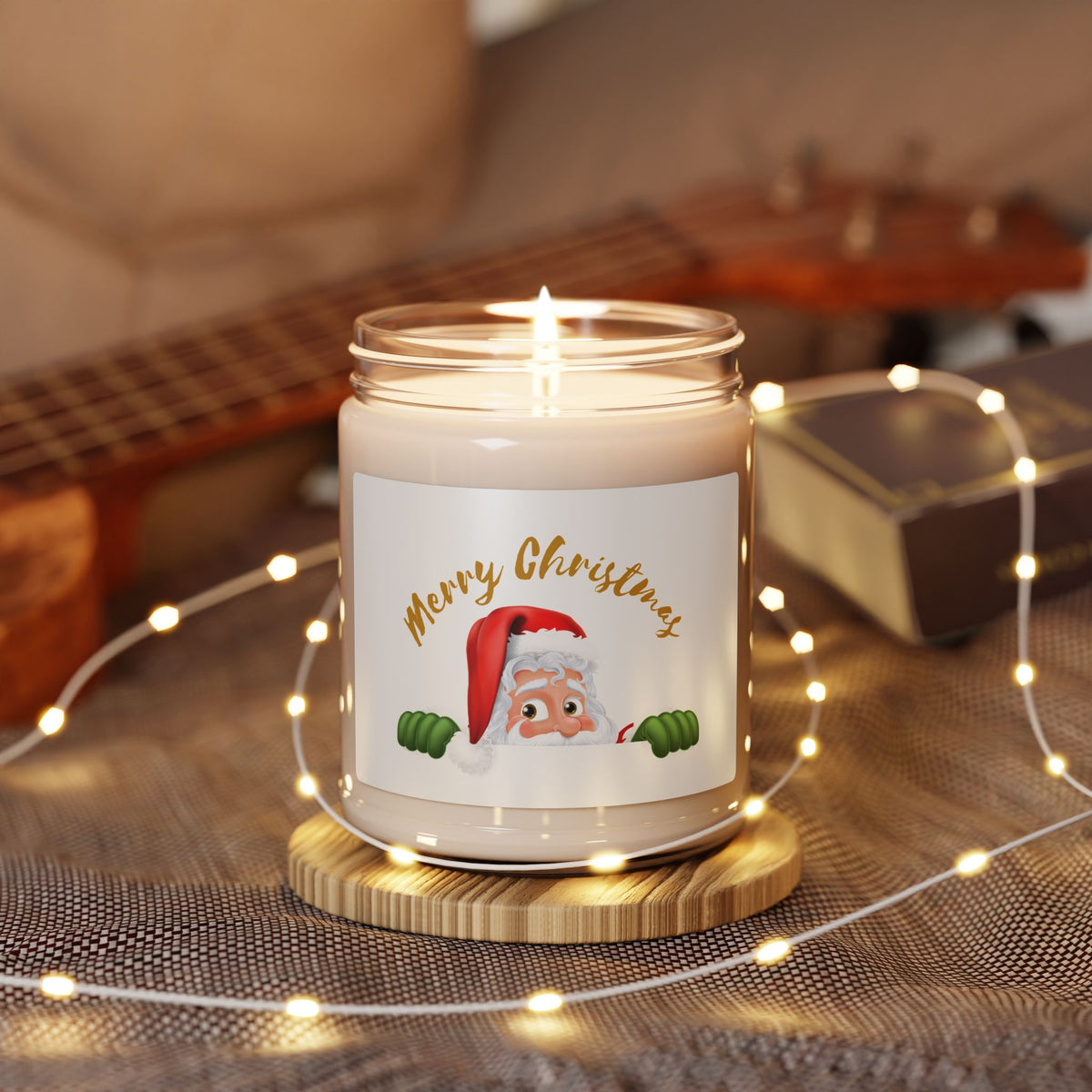 Lit soy wax glass jar Christmas candle featuring a cute peeking Santa Claus with gold Merry Christmas lettering, glowing with warm fairy lights on a rustic table.