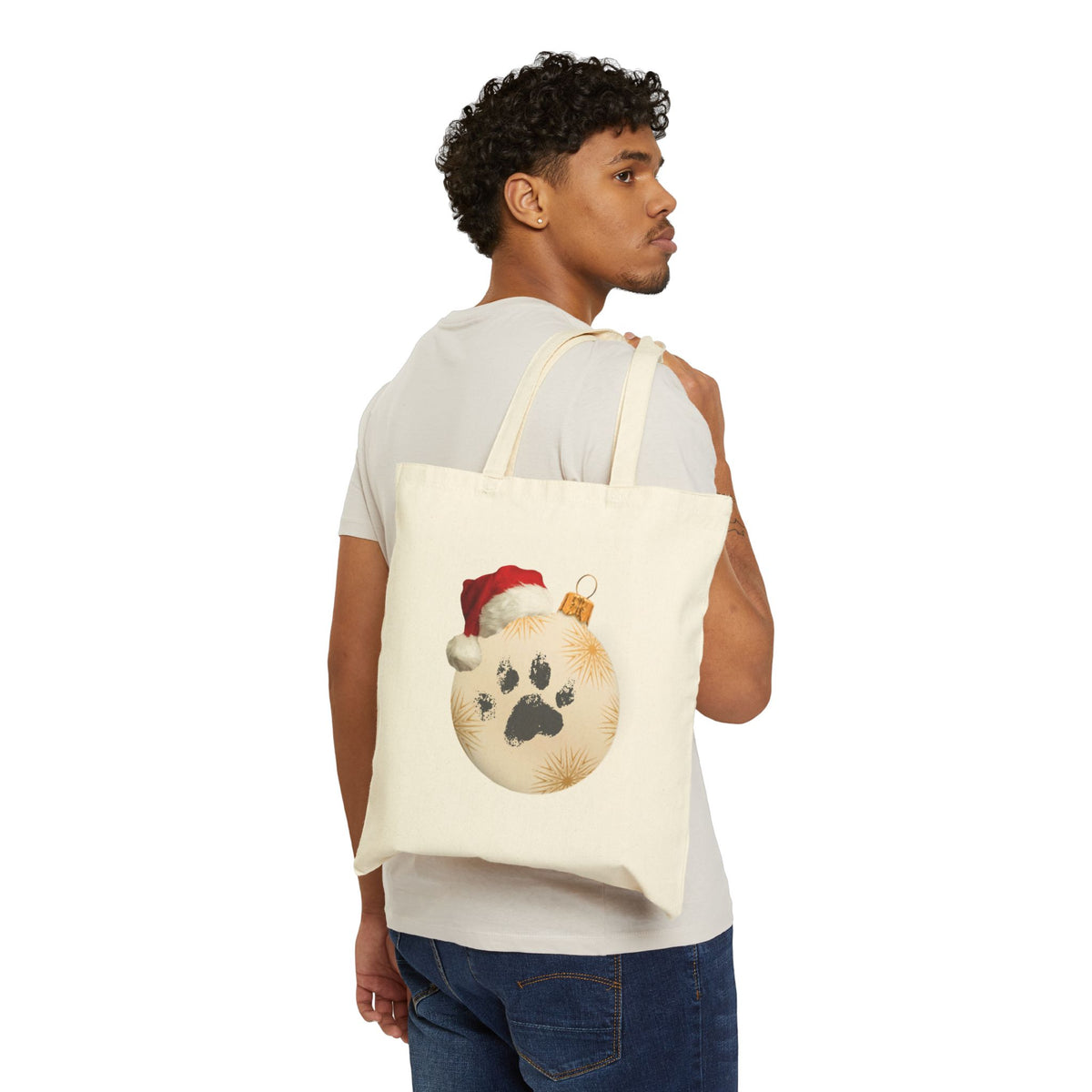Man wearing white t-shirt holding a pet lover christmas paw print ornament canvas tote bag for holiday shopping