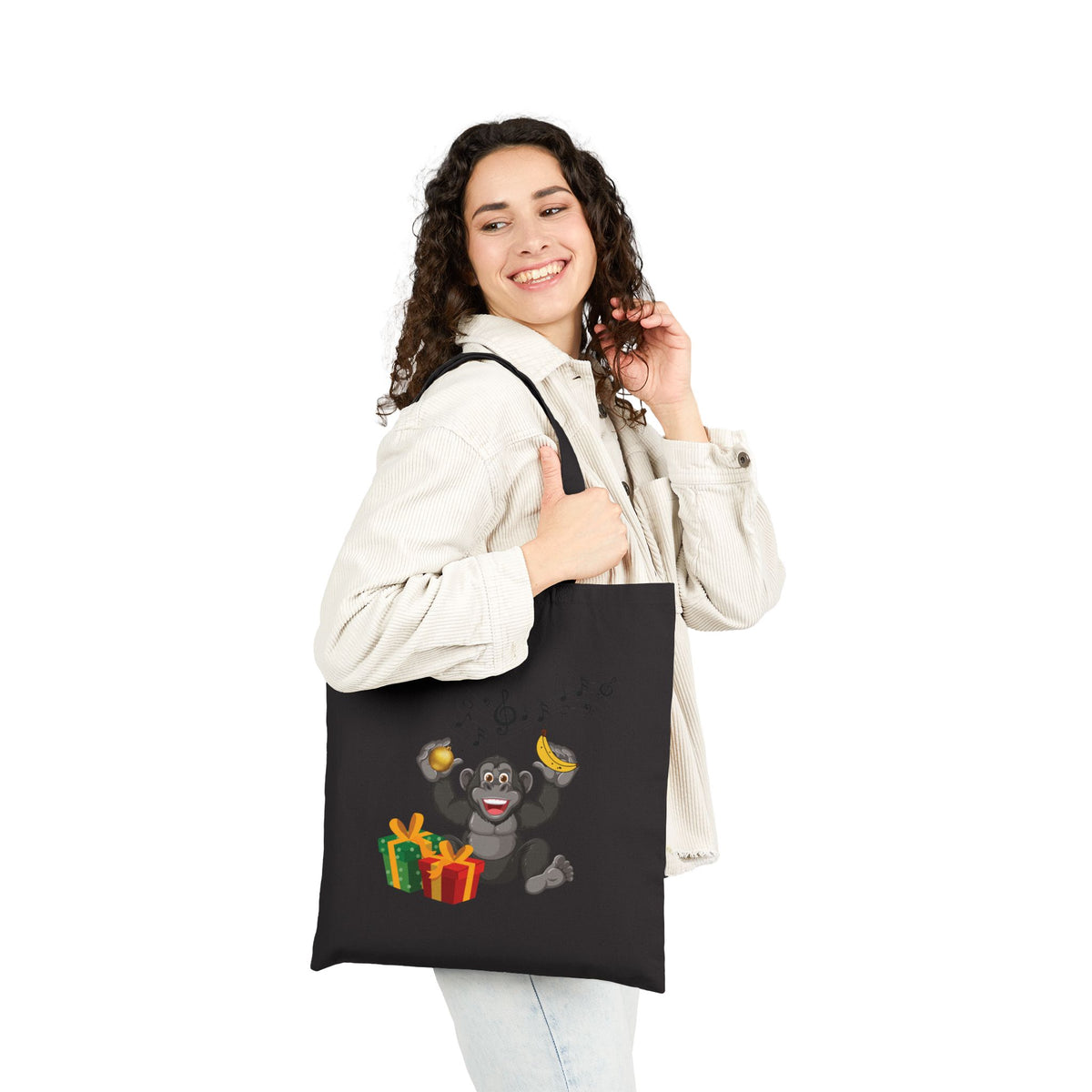 Woman wearing a black cotton tote bag printed with a playful music lover gorilla holding Christmas ornaments for casual holiday fashion.