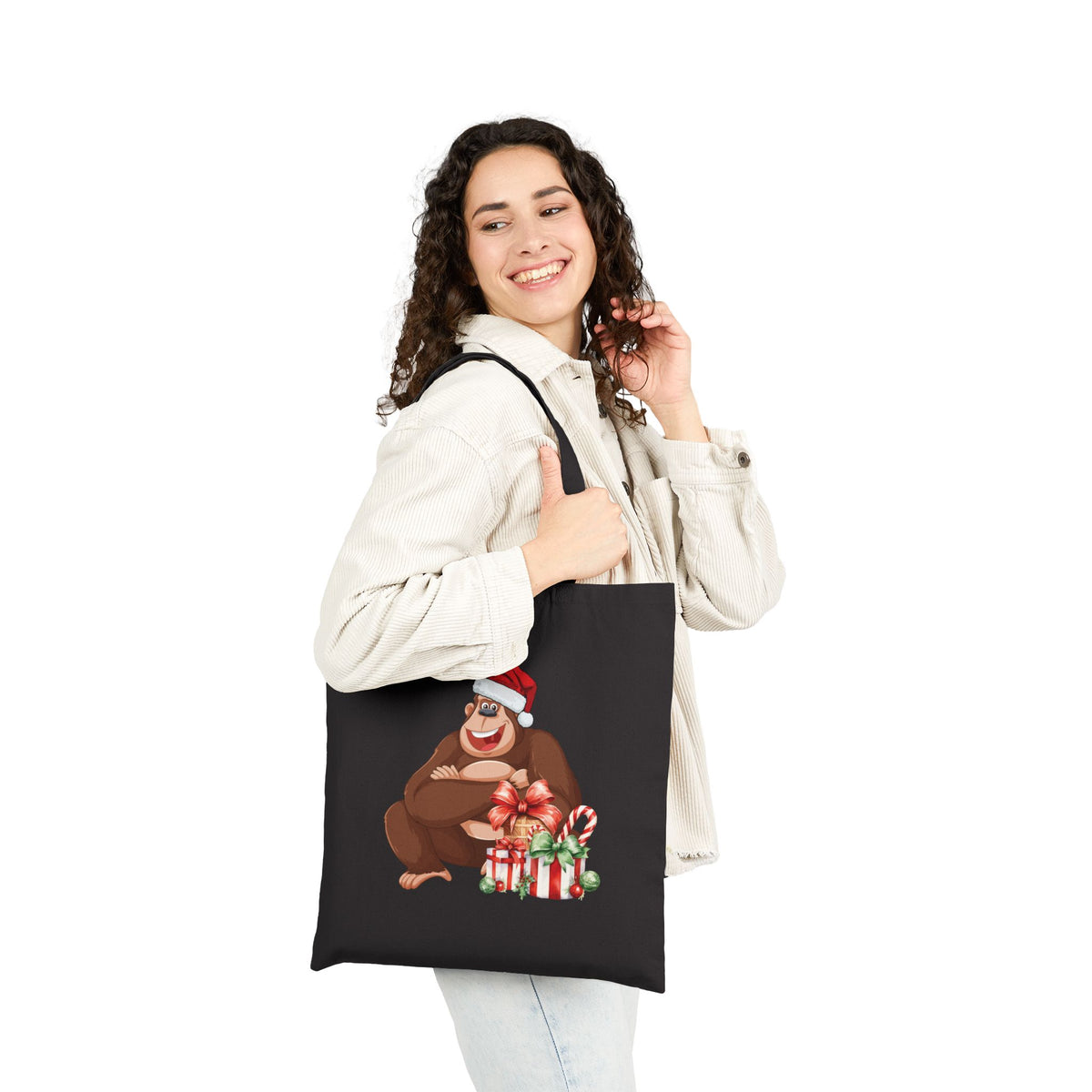 Woman wearing a black cotton tote bag printed with a cute Santa Claus gorilla holding Christmas presents for casual holiday fashion and gifting.   