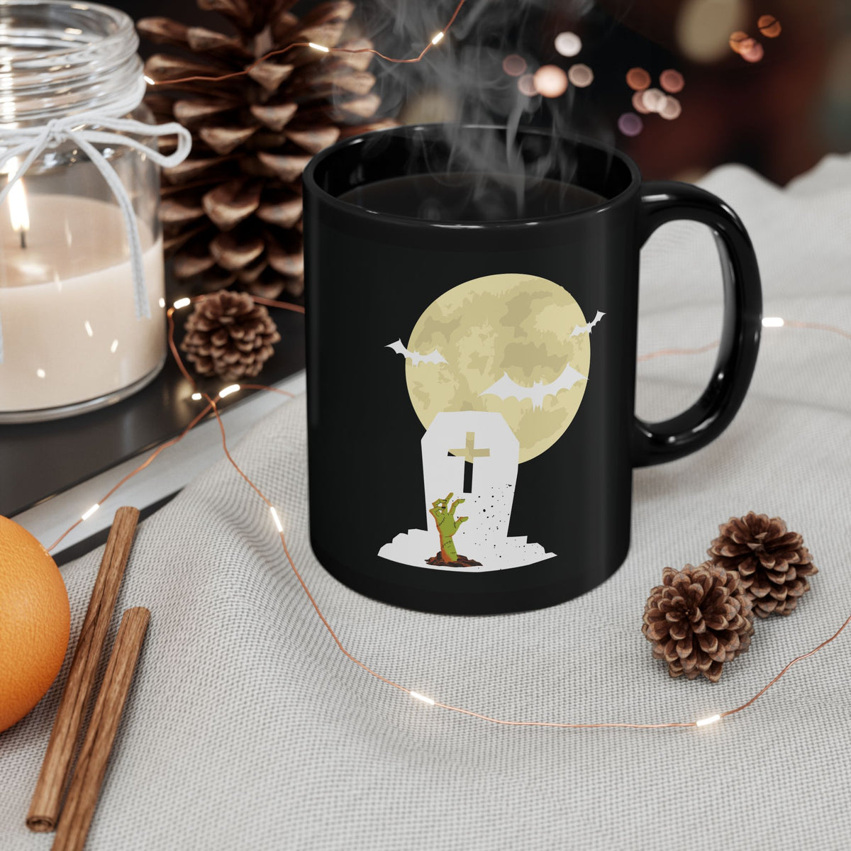 Zombie Moon spooky Halloween black ceramic coffee mug with grave hand and full moon art on cozy autumn table setup.